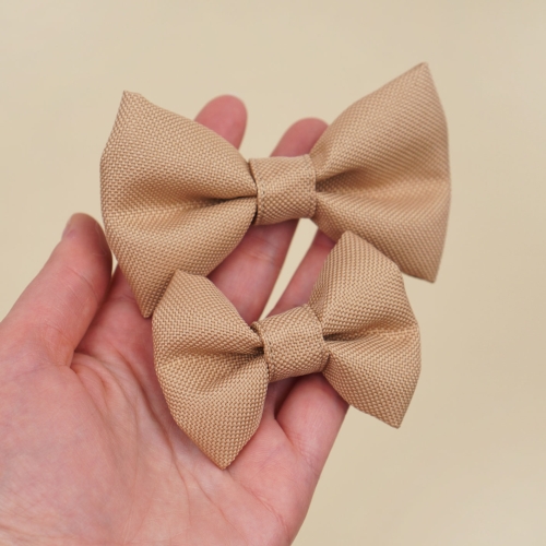 beżowa kokardka dla psa w dwóch rozmiarach S i M trzymana w dłoni