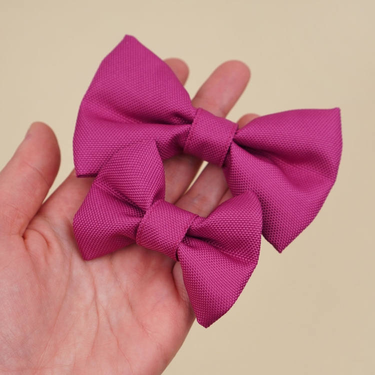 kokardka dla psa w kolorze fuksji w dwóch rozmiarach S i M trzymana w dłoni