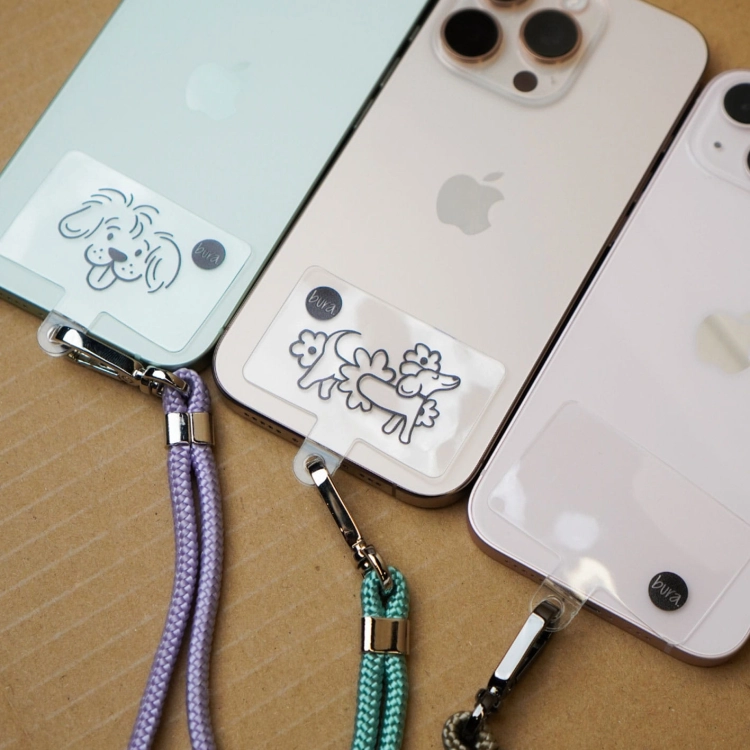 Trzy iPhone’y z wkładkami TPU Bura i zaczepionymi smyczami – różne grafiki psów, przykłady dopasowania akcesoriów.